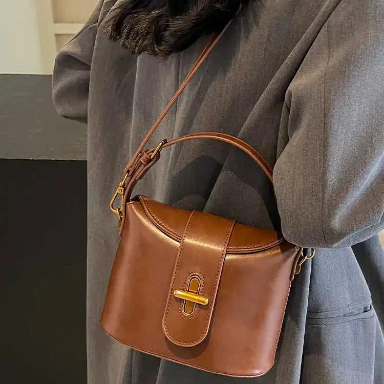 Borsa a tracolla in pelle marrone, design elegante e moderno, indossata su cappotto grigio. Accessorio moda donna, stile autunno-inverno.