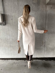 Donna di spalle con cappotto bianco elegante, stivali beige e borsa a mano, su sfondo grigio. Moda autunnale, stile sofisticato.