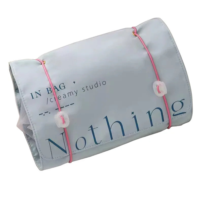 Borsa organizer da viaggio grigia con scritta "Nothing", chiusura con elastici rosa, design compatto, ideale per cosmetici e accessori.