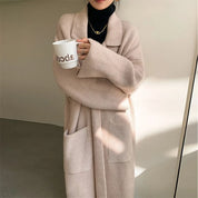Cappotto lungo beige in maglia a coste, tasche frontali, indossato su dolcevita nero. Stile casual elegante, perfetto per l'autunno inverno.