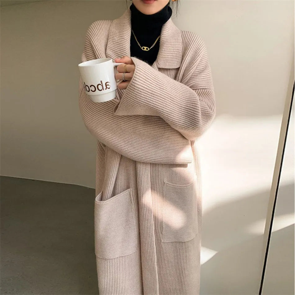 Cappotto lungo beige in maglia a coste, tasche frontali, indossato su dolcevita nero. Stile casual elegante, perfetto per l'autunno inverno.