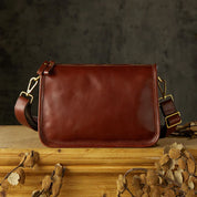 Borsa a tracolla in pelle marrone su tavolo di legno, design elegante e minimalista, accessorio moda uomo, sfondo scuro, dettagli in metallo dorato.