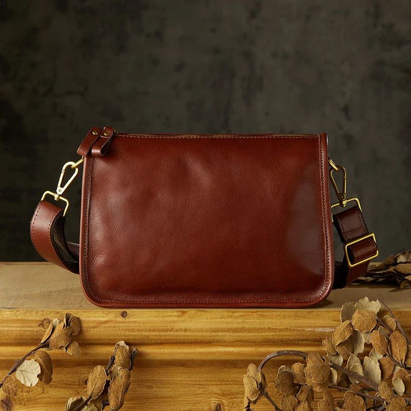 Borsa a tracolla in pelle marrone su tavolo di legno, design elegante e minimalista, accessorio moda uomo, sfondo scuro, dettagli in metallo dorato.