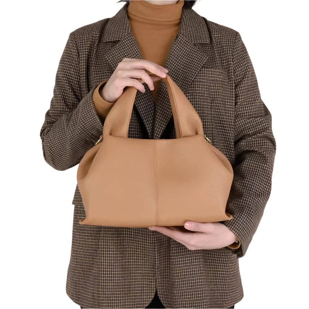 Donna con cappotto a quadri tiene borsa a mano beige in pelle, elegante e moderna. Accessorio moda femminile, perfetto per ogni occasione.