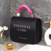 Borsa per trucco nera con scritta "Personal Care", manico rosa con perla, su lavandino in marmo. Accessori bagno, cura personale, organizer cosmetici.