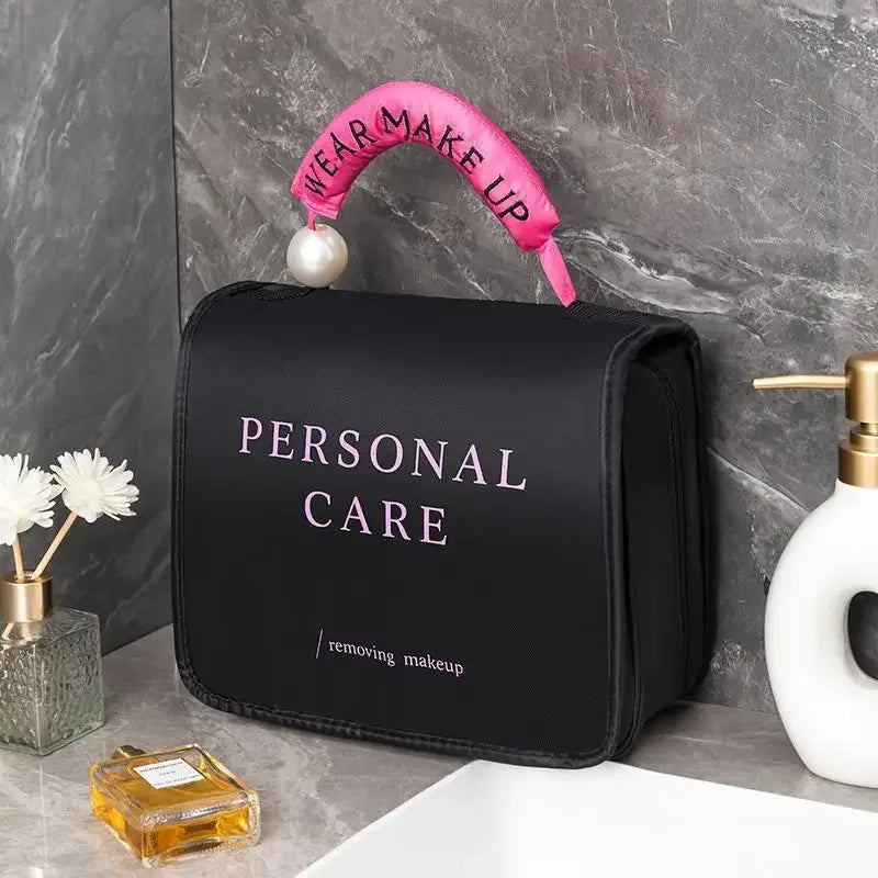Borsa per trucco nera con scritta "Personal Care", manico rosa con perla, su lavandino in marmo. Accessori bagno, cura personale, organizer cosmetici.