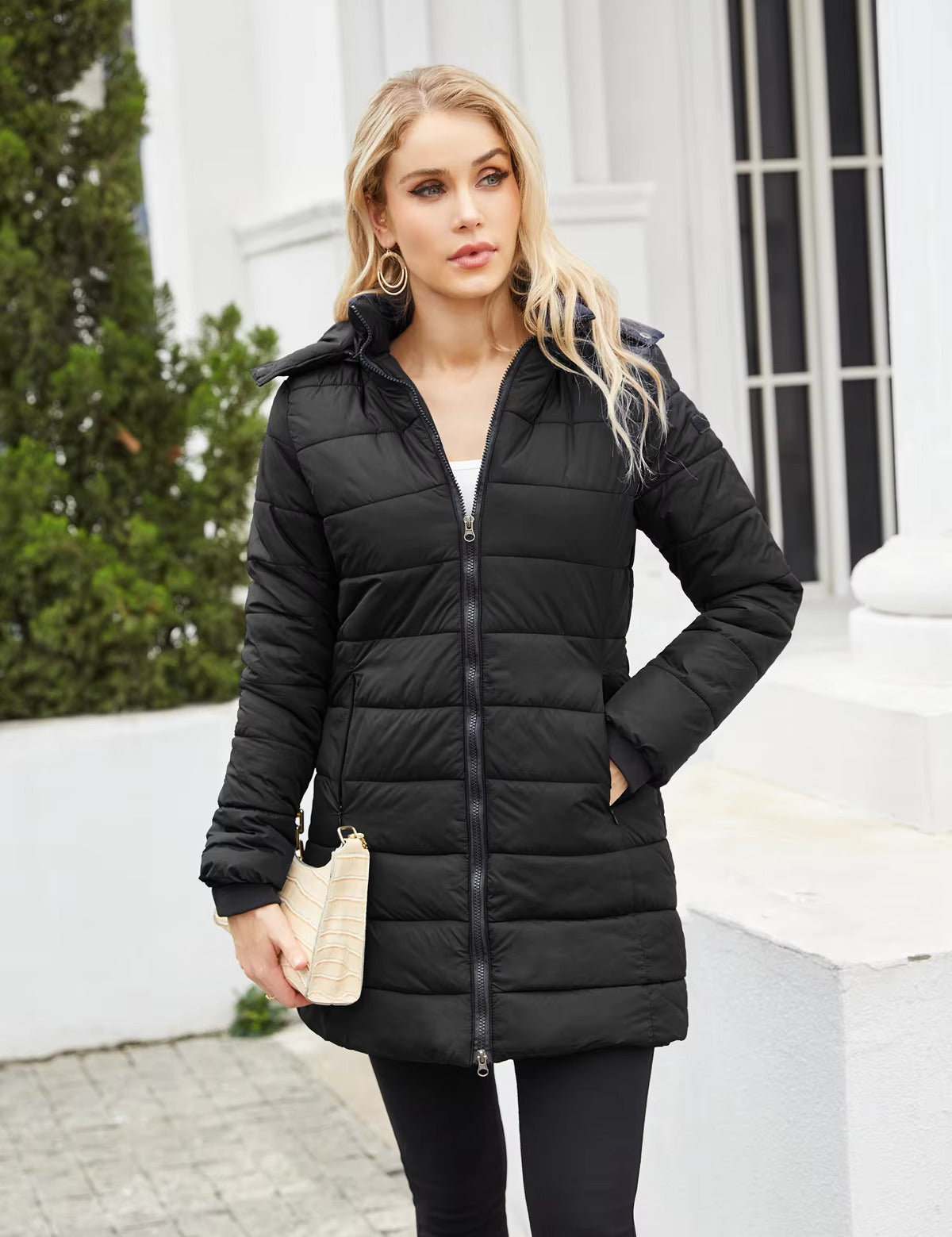 Giacca invernale nera imbottita da donna, con cappuccio, zip frontale, indossata all'aperto. Elegante e calda, ideale per l'inverno.