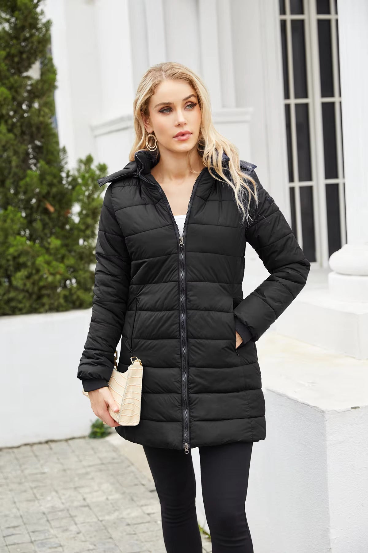 Giacca invernale nera imbottita da donna, con cappuccio, zip frontale, indossata all'aperto. Elegante e calda, ideale per l'inverno.