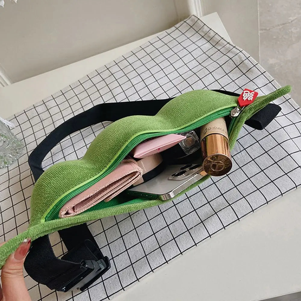 Marsupio verde aperto su tovaglia a quadri, contenente portafoglio rosa, rossetto e smartphone. Accessorio moda pratico e trendy per donna.