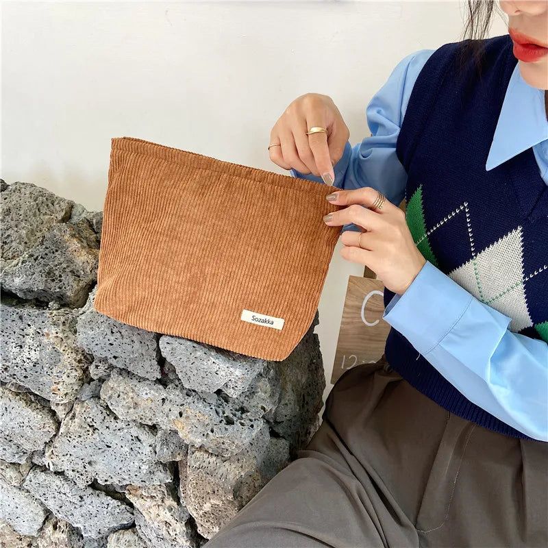 Donna con borsa a tracolla in velluto a coste marrone, su sfondo di pietra. Moda autunnale, accessori eleganti, stile casual chic.