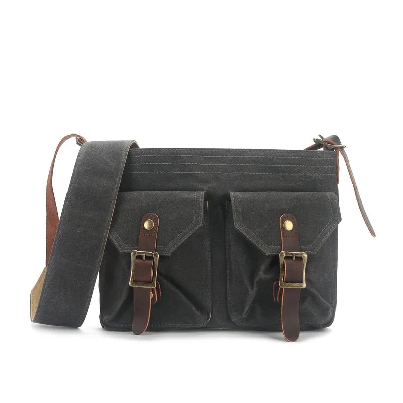 Borsa a tracolla in tela nera con doppie tasche frontali, fibbie in pelle marrone e cinturino regolabile. Stile vintage, ideale per uomo e donna.