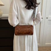 Donna con borsa a tracolla in pelle marrone con motivo floreale, indossa abito bianco. Accessorio moda elegante, stile vintage.