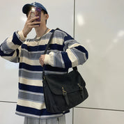 Uomo con maglia a righe blu e bianche, cappello blu, e borsa a tracolla nera. Stile casual, moda urbana, accessori maschili.
