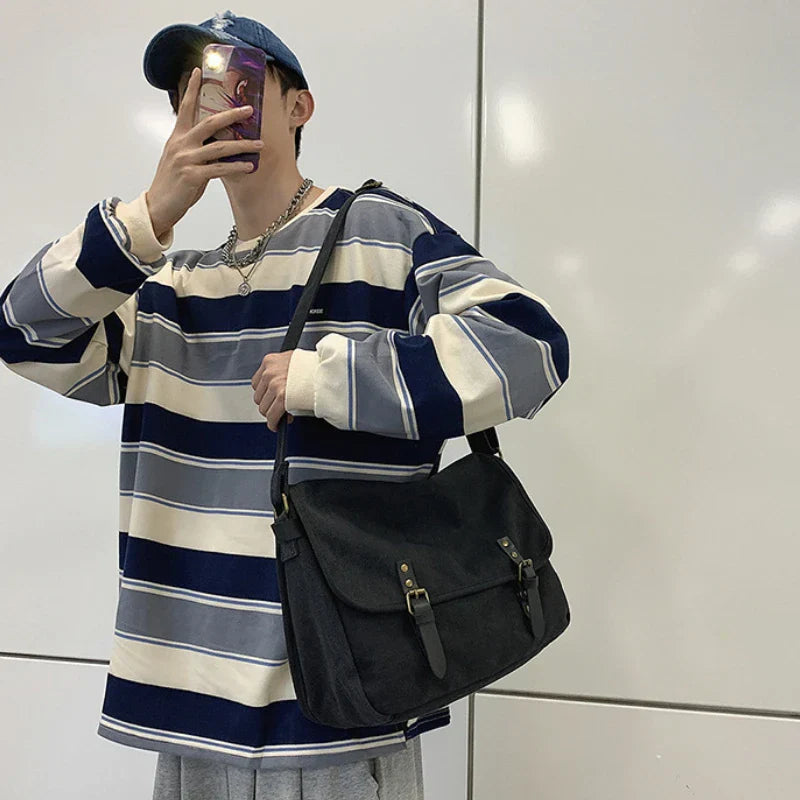 Uomo con maglia a righe blu e bianche, cappello blu, e borsa a tracolla nera. Stile casual, moda urbana, accessori maschili.
