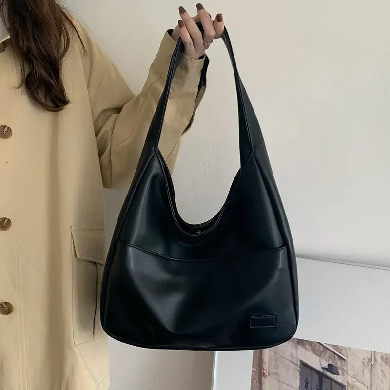 Borsa a spalla in pelle nera, design minimalista, indossata da una persona con cappotto beige. Accessorio moda elegante e versatile.