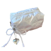 Astuccio portatrucchi bianco in raso con cerniera, decorato con fiocco di perle e ciondolo a cuore. Elegante accessorio da viaggio.