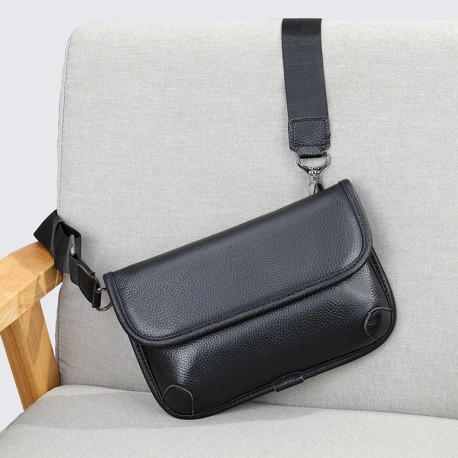 Borsa a tracolla in pelle nera su sedia grigia, design elegante e moderno, ideale per uomo e donna, accessorio moda versatile e di tendenza.