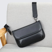 Borsa a tracolla in pelle nera su sedia grigia, design elegante e moderno, ideale per uomo e donna, accessorio moda versatile e di tendenza.