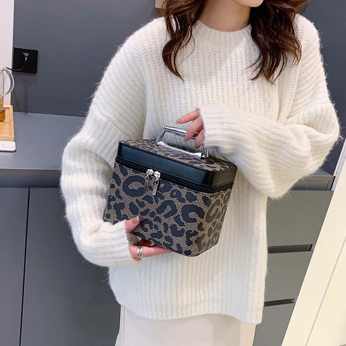 Donna con maglione bianco tiene borsa trucco leopardata con manico, design elegante e moderno, ideale per organizzare cosmetici e accessori.