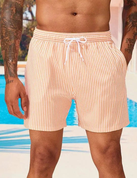 Uomo in costume da bagno a righe arancioni e bianche, in piedi vicino a una piscina. Moda estiva, abbigliamento mare, tendenze 2023.