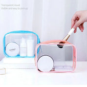 Due astucci trasparenti per cosmetici, uno blu e uno rosa, con prodotti di bellezza e pennello. Design pratico, ideale per viaggio e organizzazione.