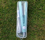 Piastra per capelli portatile verde menta in custodia trasparente su erba. Include cavo di alimentazione. Ideale per styling capelli in viaggio.