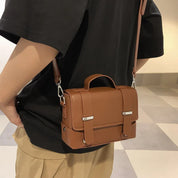 Borsa a tracolla in pelle marrone, design elegante e compatto, indossata su abbigliamento casual. Accessorio moda uomo/donna, stile urbano.
