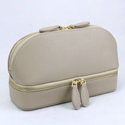 Elegante borsa cosmetica in pelle beige con doppia cerniera dorata, design compatto e moderno, ideale per organizzare trucchi e accessori da viaggio.