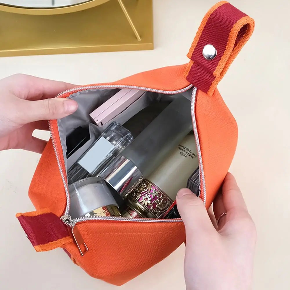 Borsa cosmetica arancione aperta, contenente trucchi e prodotti di bellezza. Design compatto, ideale per viaggi e organizzazione quotidiana.