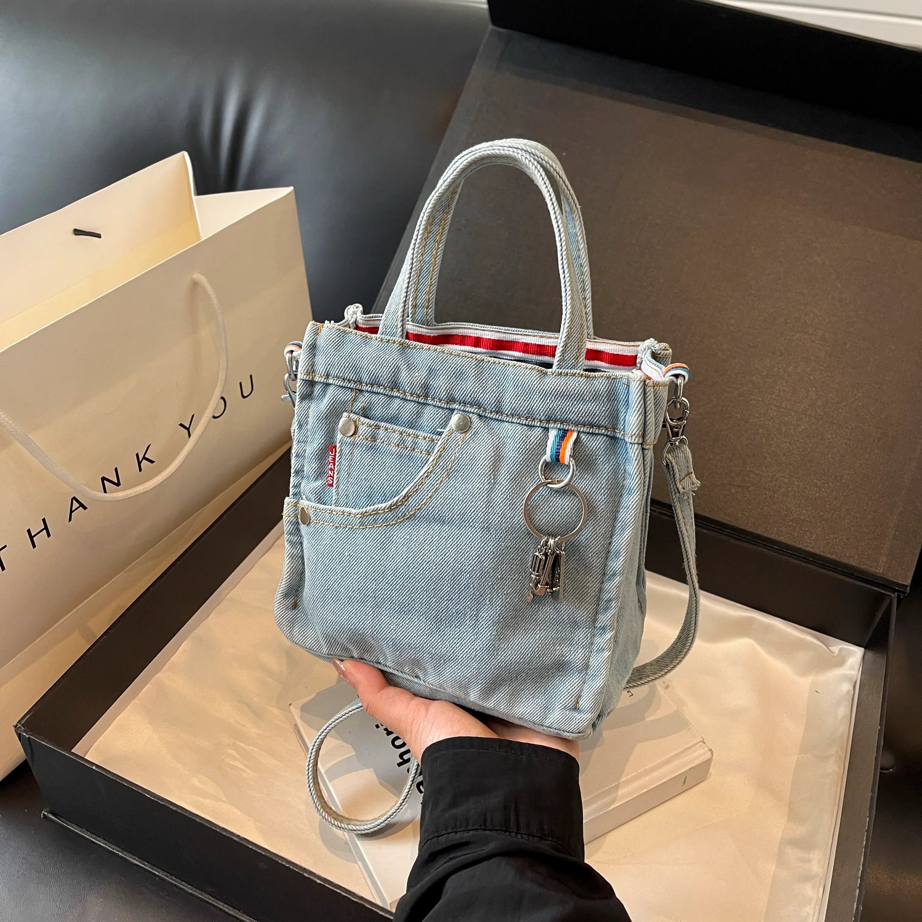Borsa a mano in denim con tasca frontale, dettagli in metallo e fodera a righe rosse. Accessorio moda casual, perfetto per lo shopping e il tempo libero.