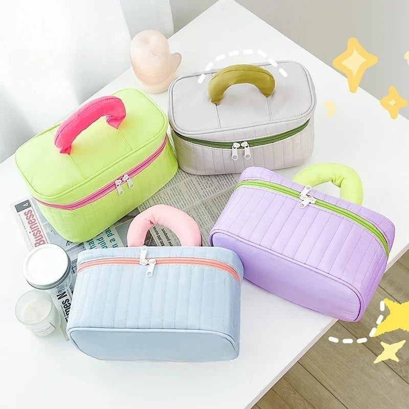 Quattro beauty case colorati con manico, in tessuto trapuntato, su tavolo bianco. Ideali per cosmetici, accessori viaggio, organizzazione.