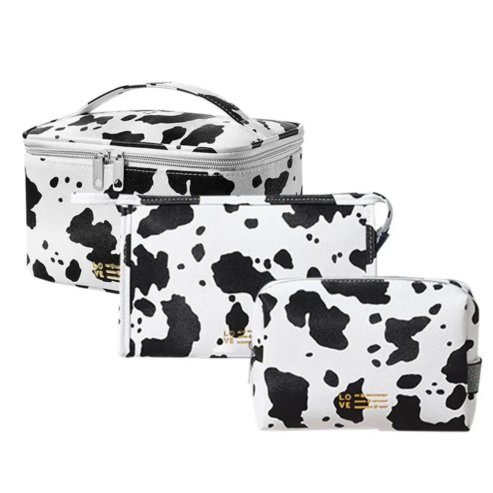 Set di tre beauty case bianchi con stampa mucca nera, chiusura a zip, ideali per viaggio e organizzazione cosmetici. Design elegante e moderno.