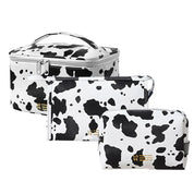 Set di tre beauty case bianchi con stampa mucca nera, chiusura a zip, ideali per viaggio e organizzazione cosmetici. Design elegante e moderno.