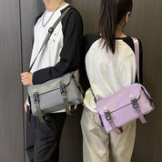 Due persone con borse a tracolla unisex, una grigia e una lilla, indossano maglie bianche e nere. Stile casual, moda urbana.