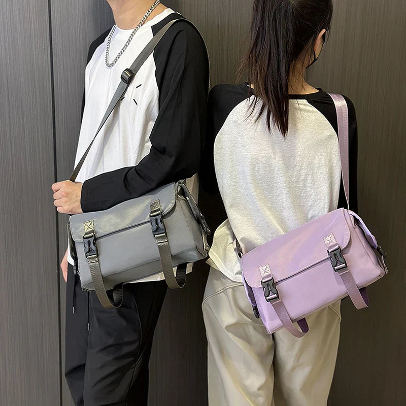 Due persone con borse a tracolla unisex, una grigia e una lilla, indossano maglie bianche e nere. Stile casual, moda urbana.