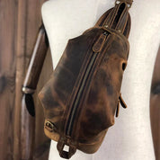 Zaino a tracolla in pelle vintage marrone, design unisex, con cerniera centrale e dettagli in metallo, ideale per viaggi e uso quotidiano.