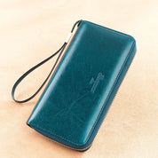 Portafoglio donna in pelle verde con cerniera, cinturino da polso, design elegante. Accessorio moda, alta qualità, ideale per organizzare carte e contanti.