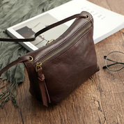 Borsa a tracolla in pelle marrone su tavolo di legno, accanto a occhiali e rivista. Elegante accessorio moda donna, stile vintage.