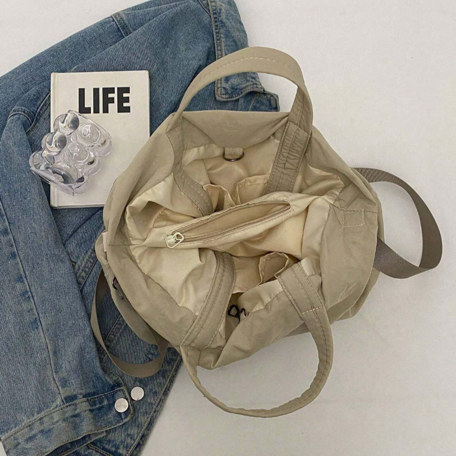 Borsa beige aperta su giacca di jeans, con libro "LIFE" e portapillole trasparente. Accessori moda casual, stile urbano, praticità quotidiana.