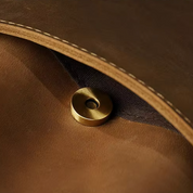 Cerniera magnetica in ottone su borsa in pelle marrone, dettaglio di alta qualità, accessorio moda elegante, chiusura sicura e resistente.