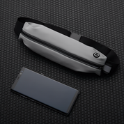 Marsupio grigio impermeabile con cerniera nera su sfondo a nido d'ape, accanto a smartphone nero. Accessorio moda pratico e moderno.