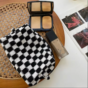 Trucco su tavolo: fondotinta liquido, cipria compatta e fascia a quadri bianchi e neri. Accessori bellezza, cosmetici, moda.