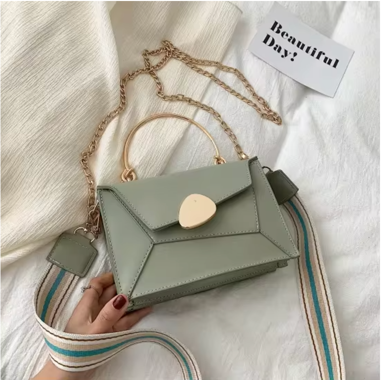 Borsa a tracolla verde salvia con manico dorato e catena, design geometrico, su tessuto bianco. Accessorio moda elegante per donna.