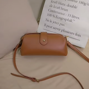 Borsa a tracolla in pelle marrone chiaro su letto beige, design elegante con chiusura a bottone dorato, ideale per moda donna e accessori casual.