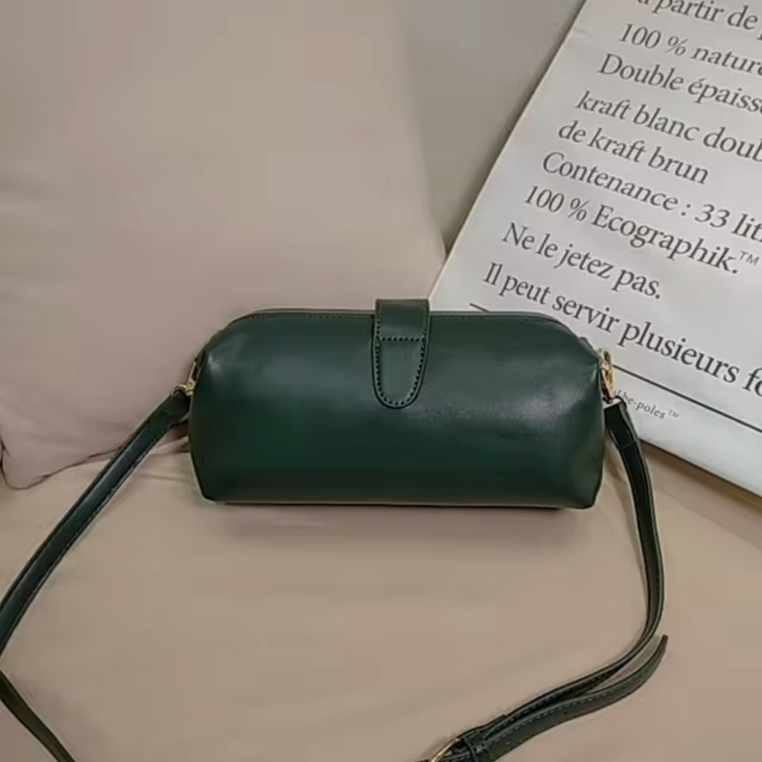 Borsa a tracolla verde scuro in pelle su divano beige, design elegante e moderno, accessorio moda donna, perfetta per ogni occasione.