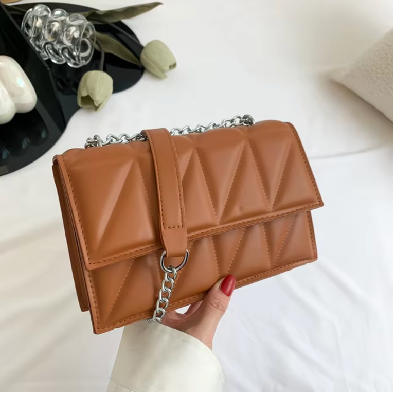 Borsa a tracolla in pelle marrone con motivo trapuntato geometrico, catena argentata, su sfondo bianco. Accessorio moda elegante e moderno.