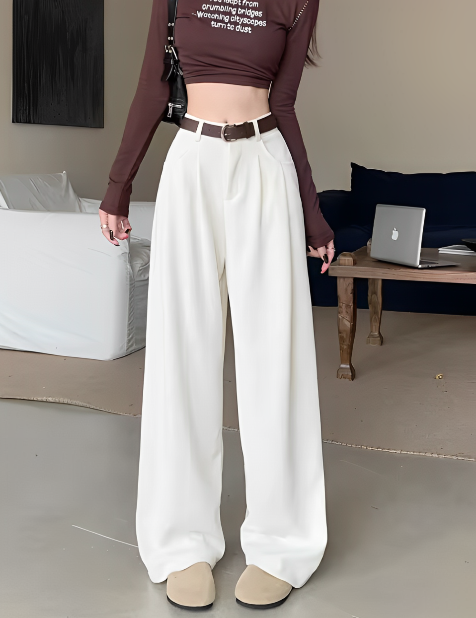 Donna con pantaloni bianchi larghi, cintura marrone e top marrone a maniche lunghe. Stile moda casual, soggiorno moderno.
