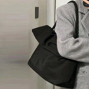 Borsa a spalla nera in tessuto, design elegante, manico intrecciato, indossata con cappotto grigio. Accessorio moda donna, stile casual chic.