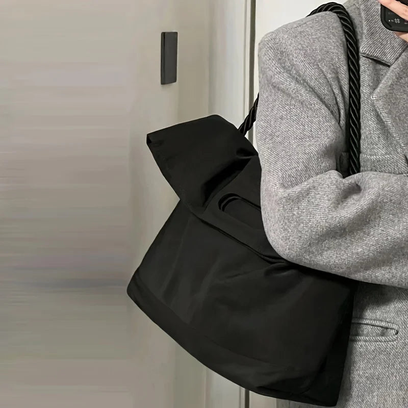 Borsa a spalla nera in tessuto, design elegante, manico intrecciato, indossata con cappotto grigio. Accessorio moda donna, stile casual chic.