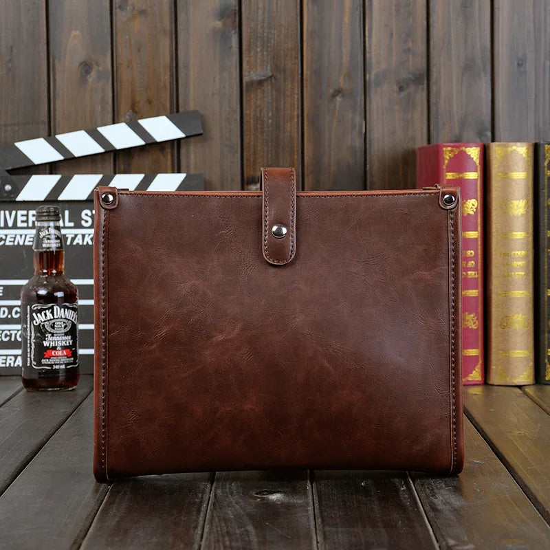 Cartella in pelle marrone su sfondo di legno, con bottiglia di whisky e libri. Elegante e resistente, ideale per lavoro e ufficio.